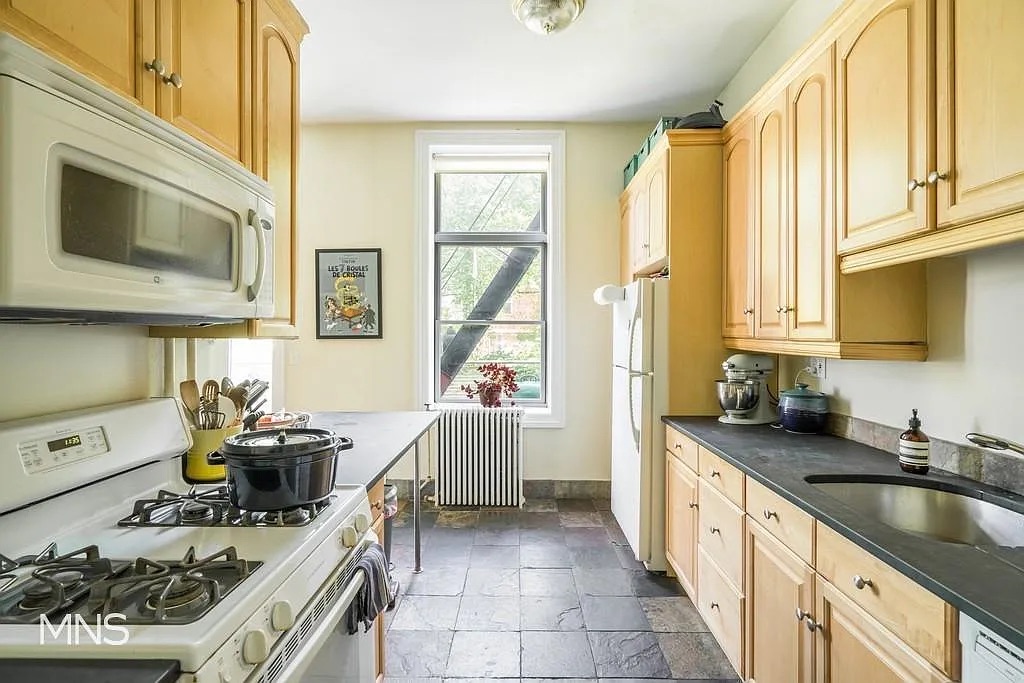 Bright kitchen featuring wooden cabinets, modern appliances, and a large window overlooking a garden.