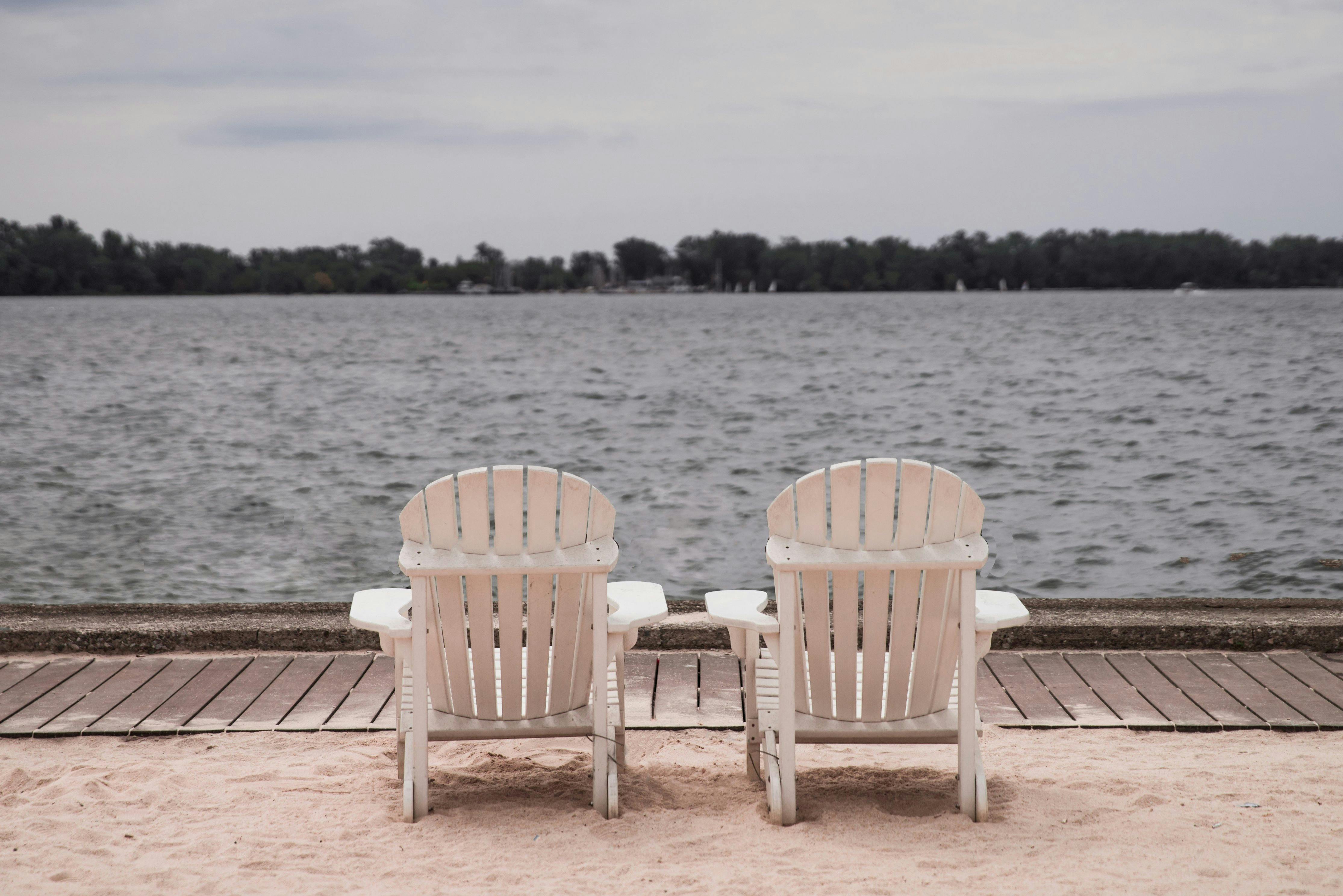 Two Adirondack chairs facing a serene water, offering a perfect relaxation spot.