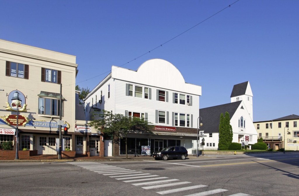 View of Main Street in Sanford, Maine, featuring mixed-use buildings, a church, and clear blue skies.