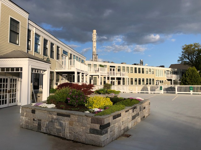 View of a multi-family apartment complex featuring well-maintained gardens and patio areas, with a cloudy sky in the background.