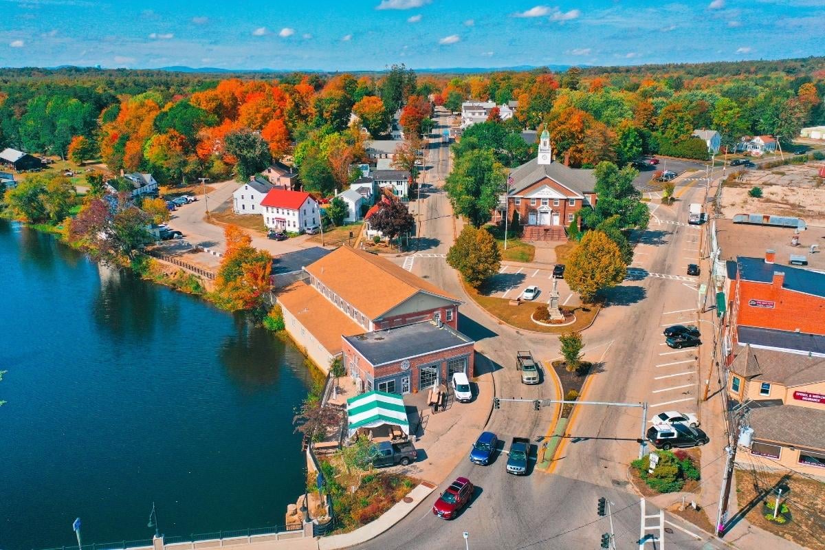 Aerial view of a charming town with colorful autumn foliage, featuring quaint buildings and a calm river.