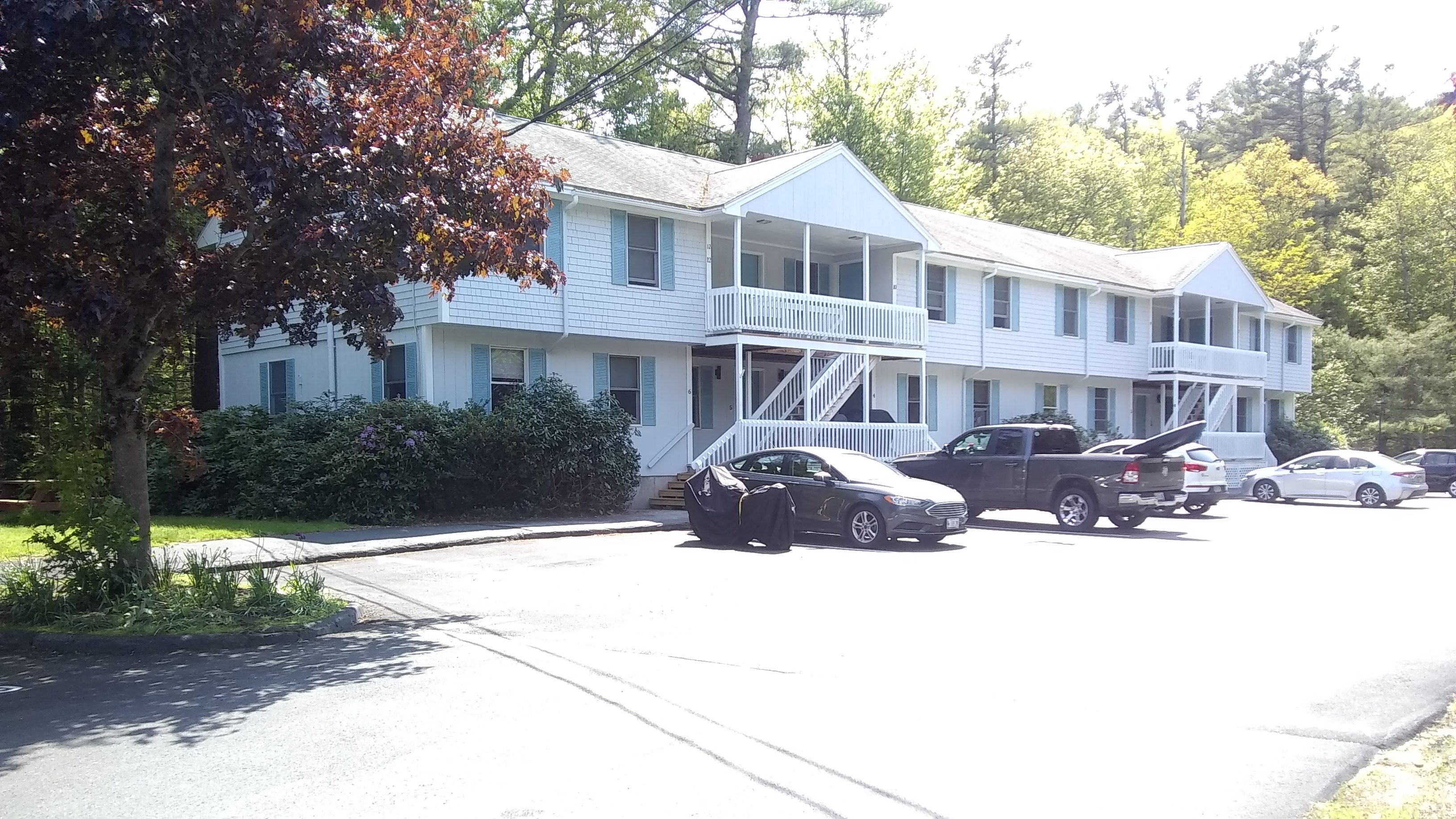 Exterior view of a multi-family apartment building in Bath, featuring a parking area with several cars and landscaping around the property.